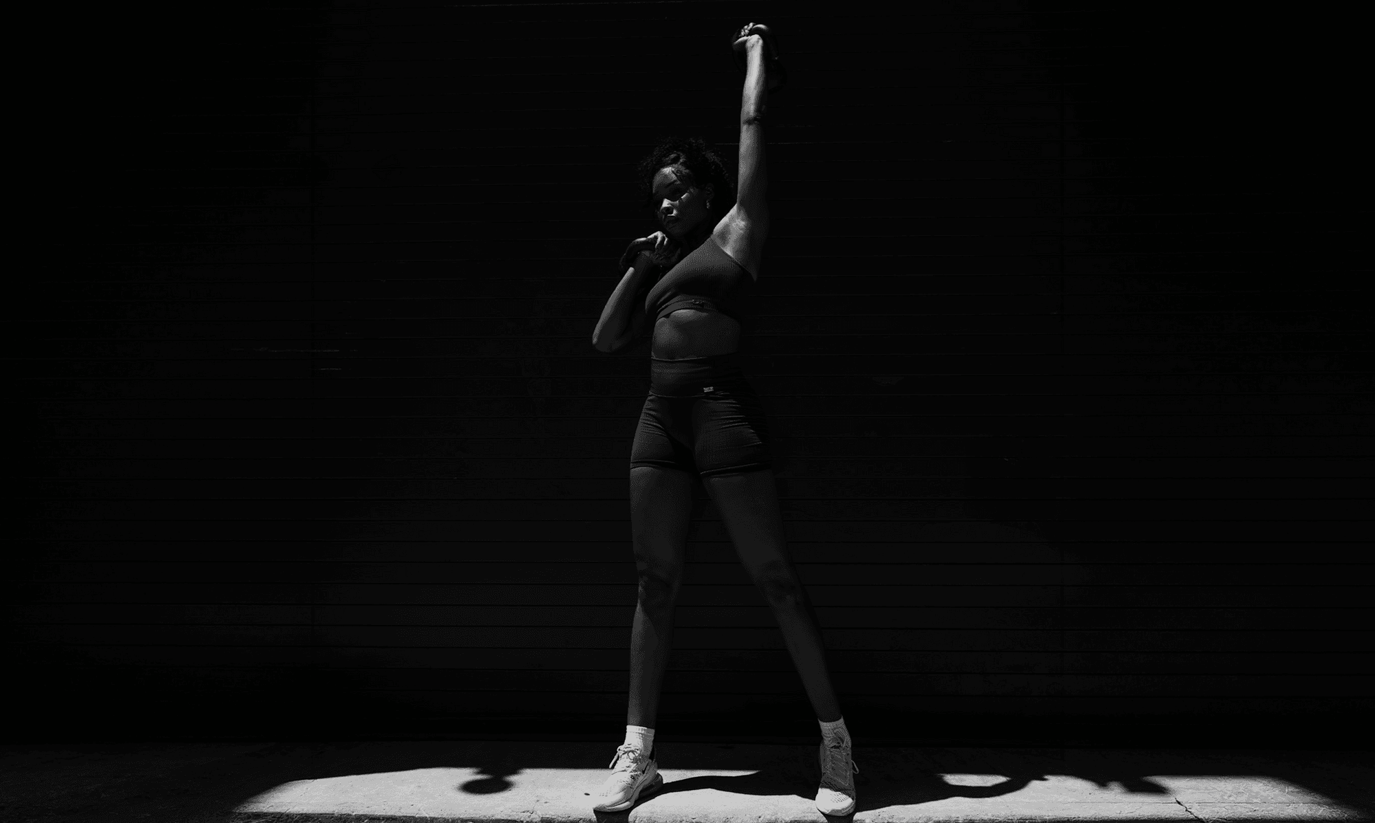 Spor salonunun önünde kettlebell ağırlığını başının üzerine kaldıran kadın sporcu.